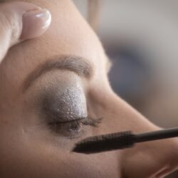person putting mascara on woman