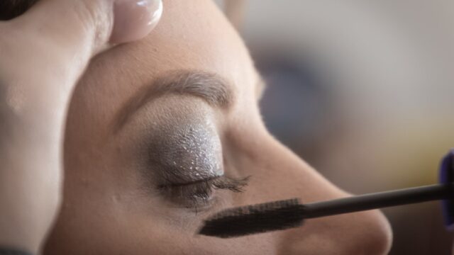 person putting mascara on woman